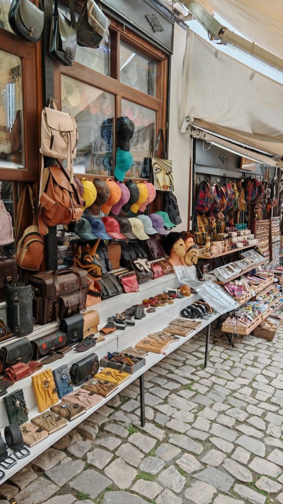 Vibrant outdoor market stall with diverse leather accessories and caps on a cobbled street.