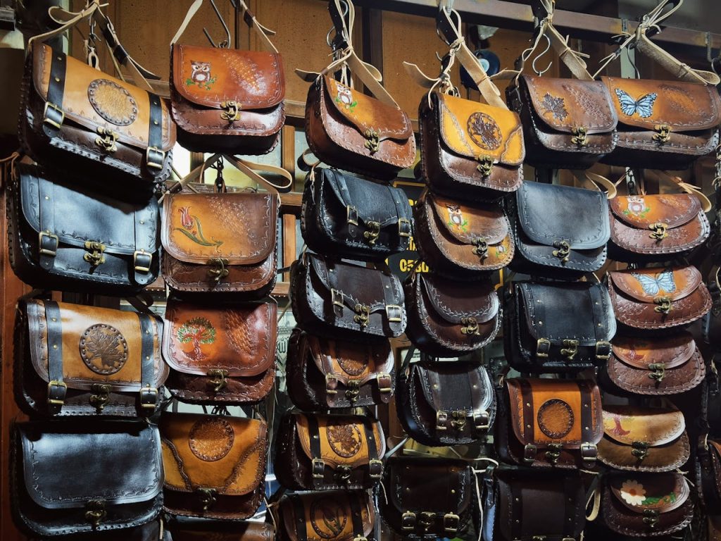A collection of handcrafted leather bags with artistic designs on display at a shop.