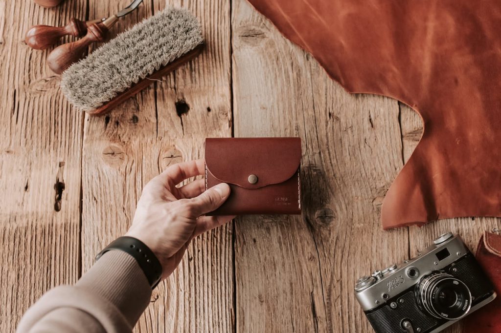 Handcrafted leather wallet on wooden surface with tools and vintage camera, showcasing artisan craftsmanship.