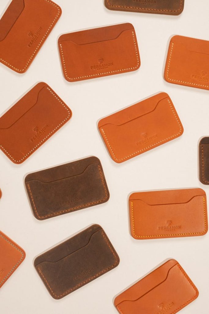 Flat lay of stylish brown and orange leather card holders on cream background.